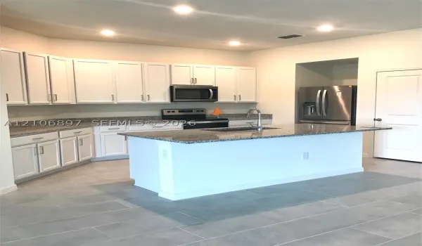 Kitchen featuring white cabinetry, stone-finish countertops, a central island with an integrated sink, recessed lighting, and large-format tile flooring