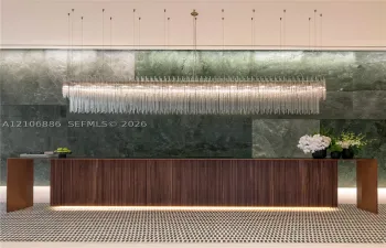 Large-scale linear chandelier with crystalline fringe, wood-veneer floating desk with base accent lighting, and full-height green-toned stone feature wall