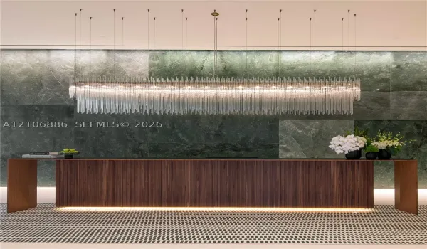 Large-scale linear chandelier with crystalline fringe, wood-veneer floating desk with base accent lighting, and full-height green-toned stone feature wall