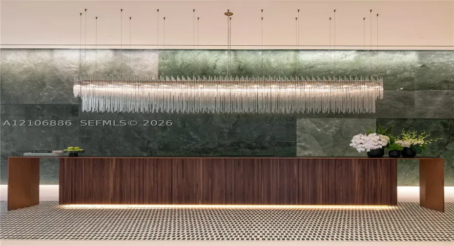 Large-scale linear chandelier with crystalline fringe, wood-veneer floating desk with base accent lighting, and full-height green-toned stone feature wall