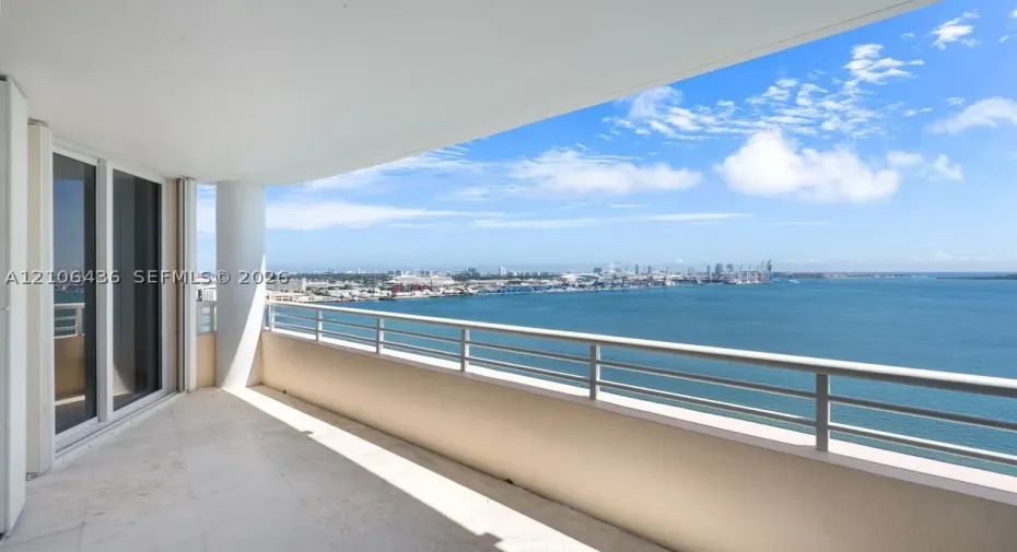Covered balcony featuring stone-finish flooring, a sleek metal railing, a structural support column, and floor-to-ceiling glass sliding doors