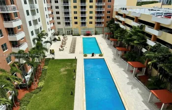 Outdoor amenity area featuring two rectangular swimming pools, stone-paved deck, manicured lawn, and multiple shaded cabanas