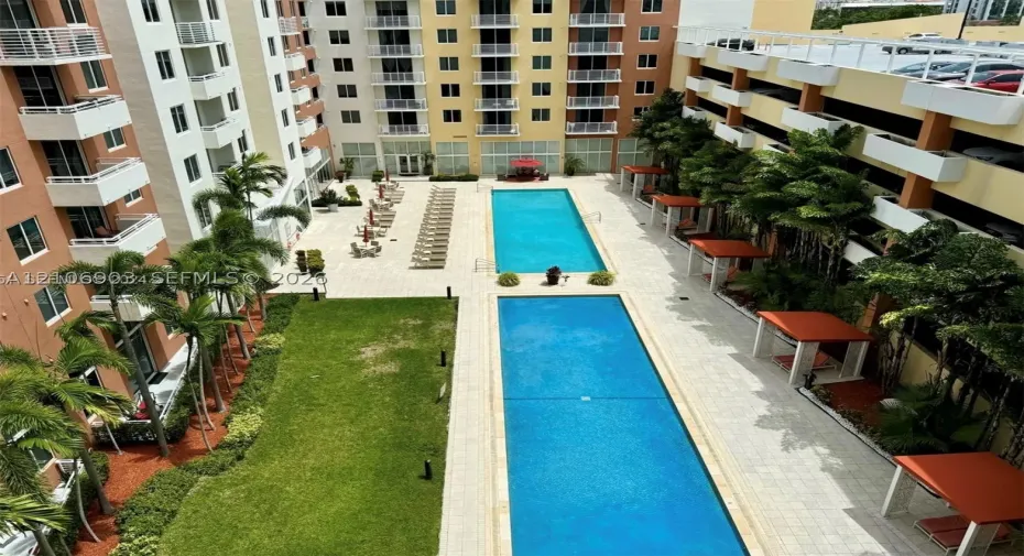 Outdoor amenity area featuring two rectangular swimming pools, stone-paved deck, manicured lawn, and multiple shaded cabanas