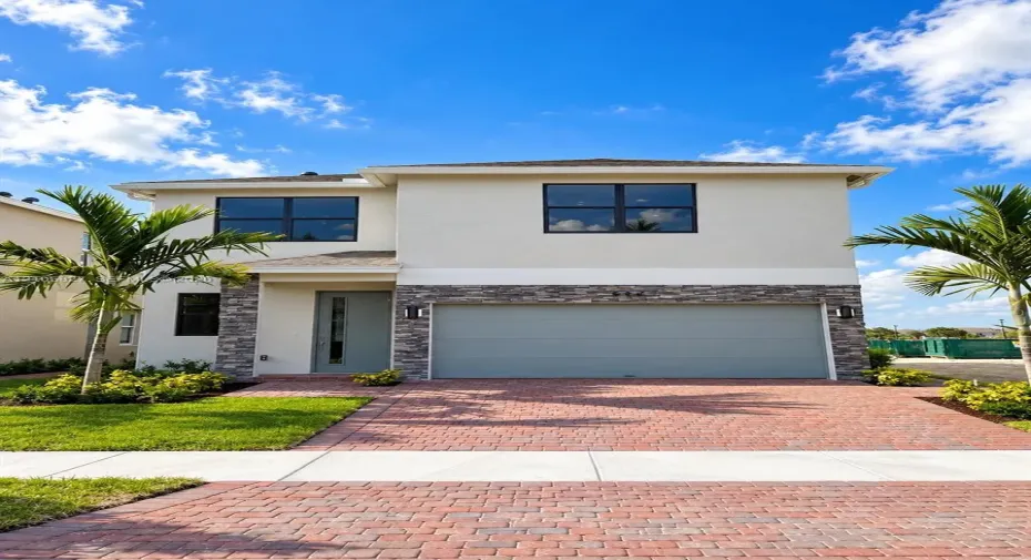 Two-story exterior featuring a light-toned stucco facade, stone veneer accents, a paver driveway, and a two-car garage