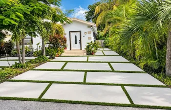 Exterior facade featuring white stucco walls, decorative quoins, a white paneled front door with glass inlay, and a concrete paver driveway with integrated turf strips
