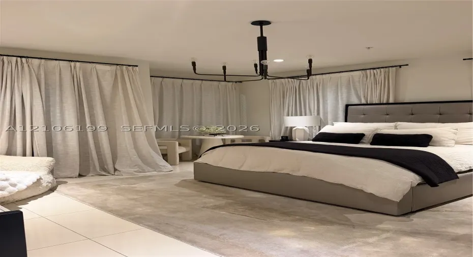 Spacious room featuring light-toned tile flooring, floor-to-ceiling drapery panels on black hardware, and a multi-arm geometric chandelier with a black finish