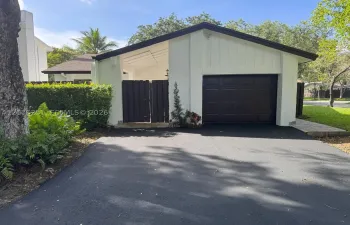 Exterior featuring a paved asphalt driveway, an attached garage with a dark-toned door, a covered entry with wood-slat screening, and low-maintenance landscaping
