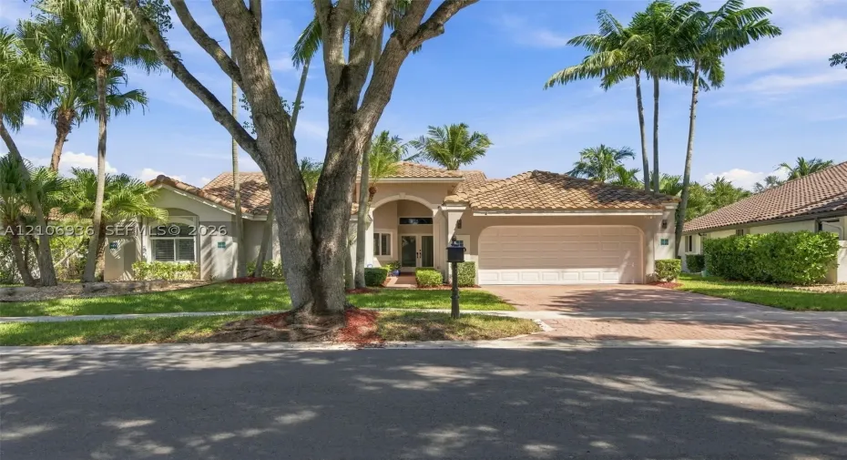 Single-story residence featuring a tile roof, arched entryway, multi-car garage, and a paver driveway