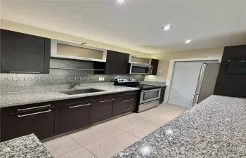 Kitchen featuring modern cabinetry, stone-finish countertops, subway tile backsplash, stainless steel appliances, and large-format tile flooring