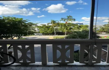 Screened balcony featuring decorative white geometric railing and tiled flooring, overlooking mature palm trees and green space
