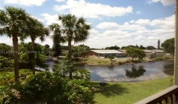 Waterfront property featuring a private canal, mature palm trees, expansive lawn, and single-story masonry residence