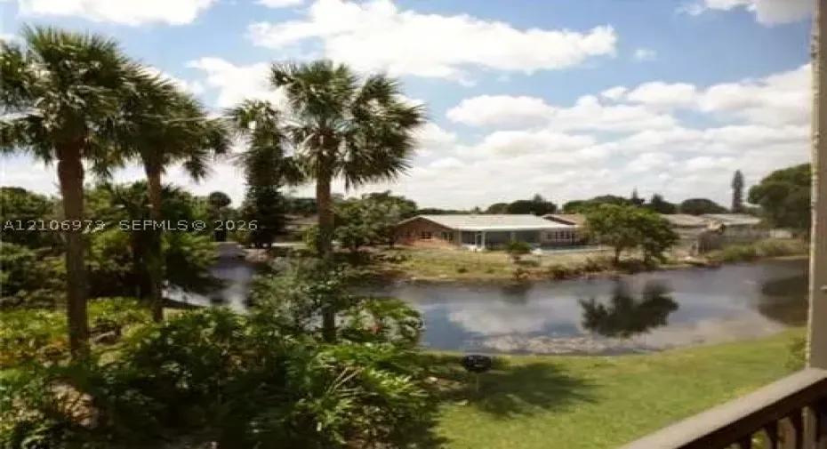 Waterfront property featuring a private canal, mature palm trees, expansive lawn, and single-story masonry residence