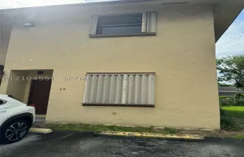 Two-story stucco exterior featuring corrugated metal storm shutters and a recessed entryway