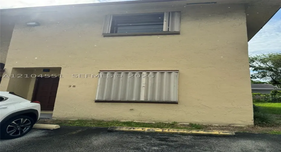 Two-story stucco exterior featuring corrugated metal storm shutters and a recessed entryway