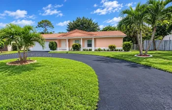 Single-story residence featuring a tile roof, covered front entrance with structural columns, and an expansive paved circular driveway situated on a landscaped lot with palm trees