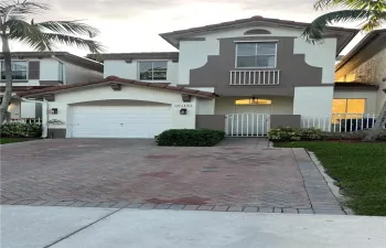 Two-story exterior featuring a stucco finish, arched entryway, a single-car garage, and a herringbone-patterned paver driveway