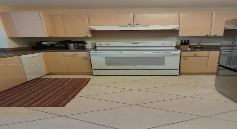 Kitchen featuring light-finish cabinetry, neutral solid-surface countertops, white electric range with overhead ventilation, and diagonal-set floor tile