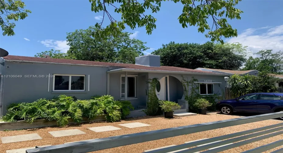 Single-story exterior featuring a arched entryway, grey smooth-finish siding, gravel landscaping, and concrete paver walkway