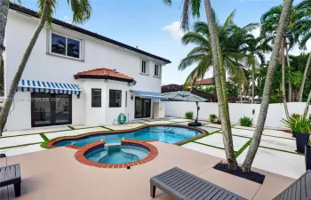 Exterior rear featuring a stucco facade, swimming pool with an attached spa, paver patio with turf inlays, and striped retractable awnings