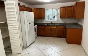 Kitchen featuring wood cabinetry, stone-finish countertops, tile flooring, a built-in pantry with louvered doors, and a stainless steel sink