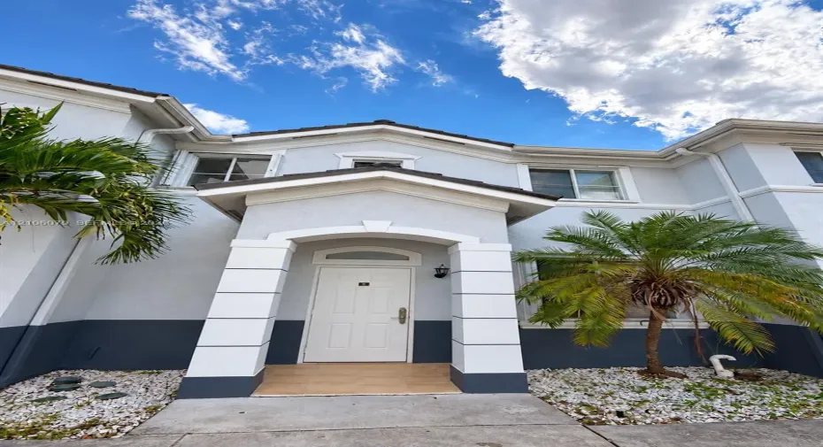 Exterior facade featuring a two-tone stucco finish, a covered entryway with structural columns, and decorative arched molding above the door