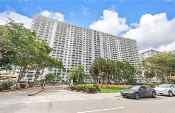 High-rise residential exterior featuring private balconies, concrete construction, paved vehicular entrance, and mature landscaping