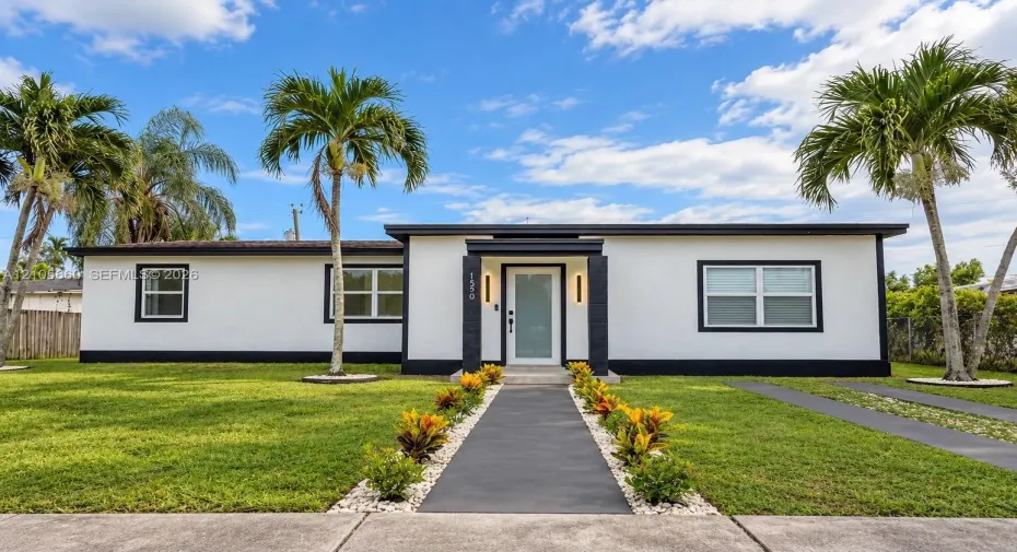 Single-story exterior featuring a high-contrast stucco facade, flat roofline, central recessed entryway with modern vertical lighting, and manicured landscaping with mature​​‌​​​​‌​​‌‌​‌‌​​​‌‌​‌​‌​‌​​​‌​​ palms