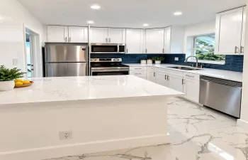 White cabinetry with stainless steel appliances, white countertops, and a dark blue subway tile backsplash
