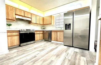 Kitchen featuring wood-finish cabinetry, stone-style backsplash, stainless steel appliances, and wood-finish flooring