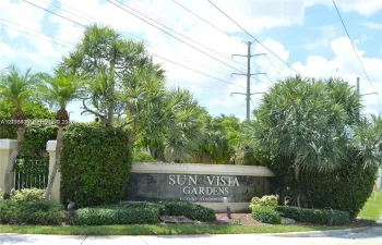 Stone monument sign featuring metallic lettering and integrated landscape lighting, surrounded by mature palm trees and manicured shrubbery