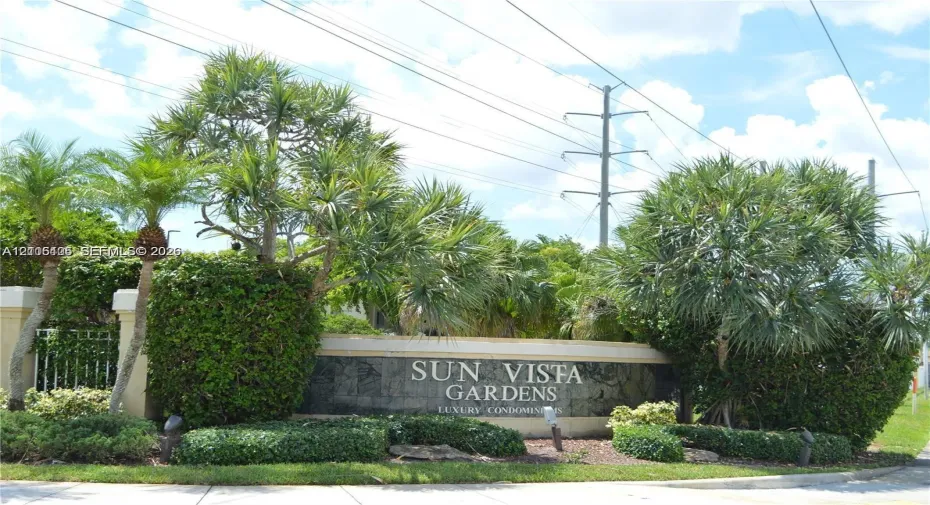 Stone monument sign featuring metallic lettering and integrated landscape lighting, surrounded by mature palm trees and manicured shrubbery