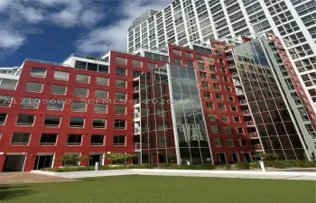 Contemporary multi-story exterior featuring a red masonry facade, floor-to-ceiling glass paneling, tiered balcony levels with glass railings, and a landscaped ground-level courtyard with synthetic turf and integrated planters