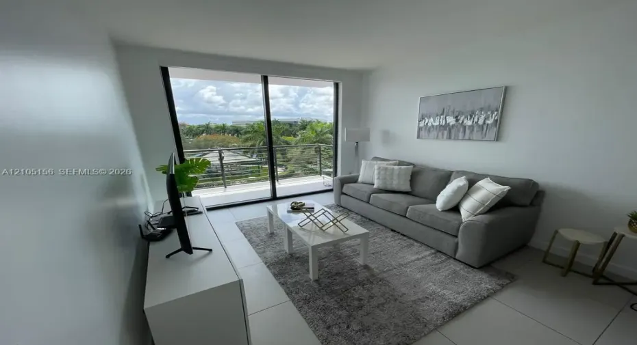 Floor-to-ceiling sliding glass doors, neutral tile flooring, and private balcony with horizontal railing