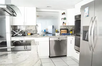 Kitchen featuring white cabinetry, stone countertops, integrated stainless steel appliances, open shelving, and tile flooring