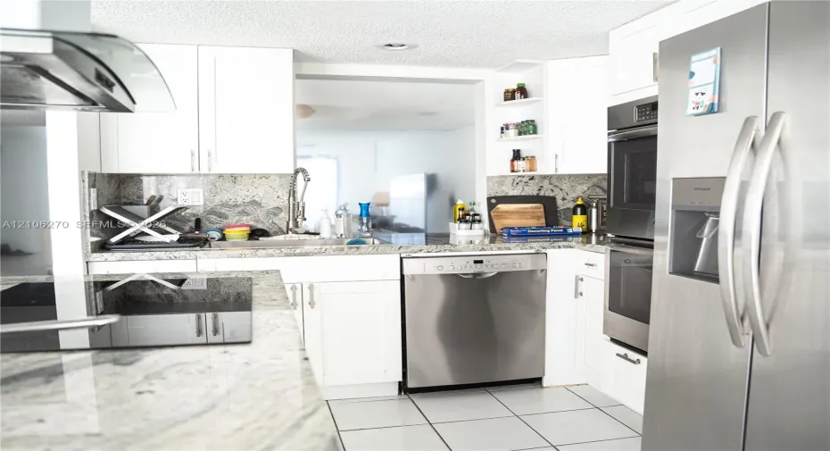 Kitchen featuring white cabinetry, stone countertops, integrated stainless steel appliances, open shelving, and tile flooring