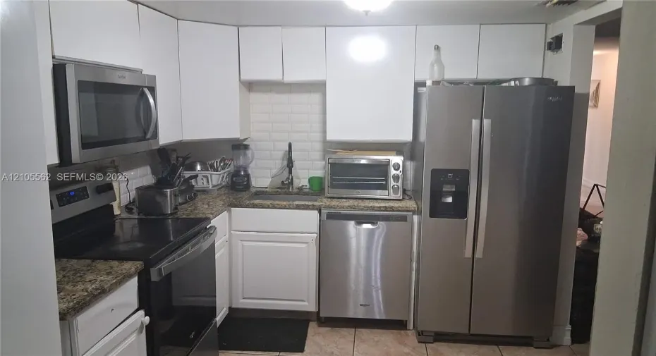Kitchen featuring white cabinetry, stainless steel appliances, speckled stone-finish countertops, and a white subway tile backsplash