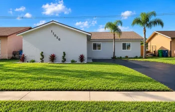 Stucco exterior with a pitched shingle roof, complemented by a paved driveway, mature palm trees, and manicured landscaping