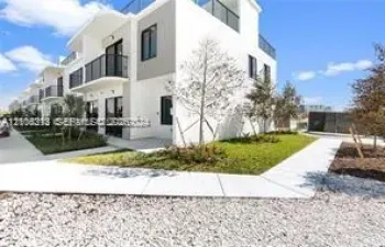 Modern multi-level exterior featuring white stucco facade, glass-paneled balcony railings, and concrete walkways