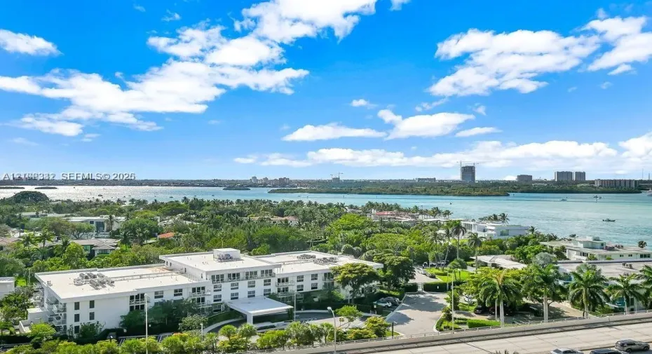 Aerial perspective of coastal property featuring multi-story white building, lush tropical landscaping, paved motor court, and extensive water frontage