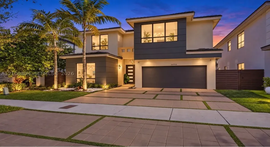 Two-story contemporary exterior featuring stucco siding, multi-pane picture windows, a paved geometric driveway, and an attached two-car garage