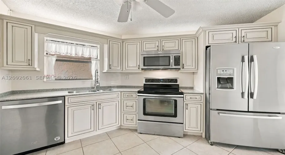 Kitchen featuring light-toned cabinetry, stainless steel appliances, speckled stone-finish countertops, and tile flooring