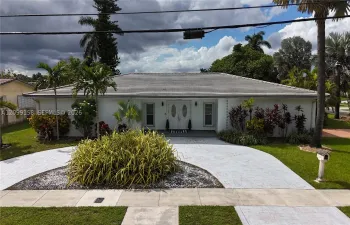 Stucco exterior featuring a double-door entry, hip roof, and circular paved driveway set within landscaped grounds