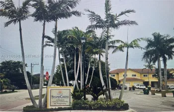 Stone Creek community entrance featuring mature palm trees, professional landscaping, a monument sign, and asphalt paving