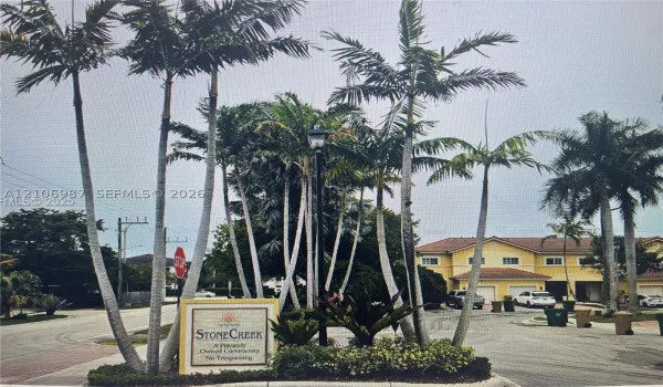 Stone Creek community entrance featuring mature palm trees, professional landscaping, a monument sign, and asphalt paving