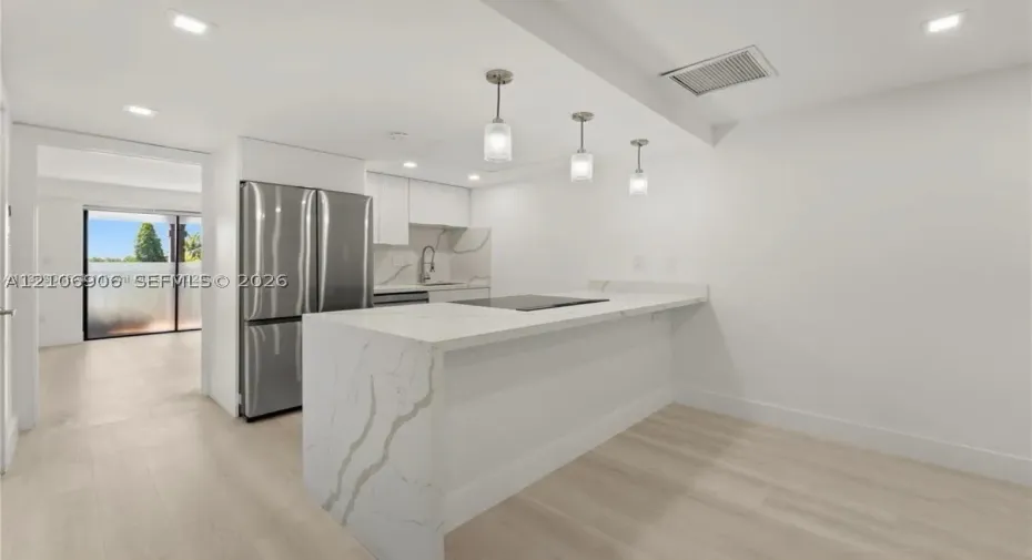 Kitchen featuring a stone-surface waterfall island, stainless steel refrigerator, recessed lighting, pendant fixtures, and wood-finish flooring