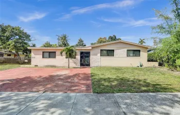 Single-story residence featuring a painted masonry exterior with textured stone facade detailing, a low-pitch roofline, and a paved hexagonal-patterned driveway