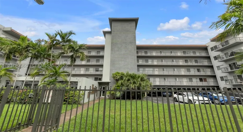 Multi-story exterior featuring a gray stucco facade, tiered balconies with metal railings, and a fenced perimeter