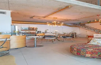 Industrial-style loft featuring an exposed concrete ceiling, open-tread staircase, large-format tile flooring, metallic exposed ductwork, and a multi-arm brass light fixture