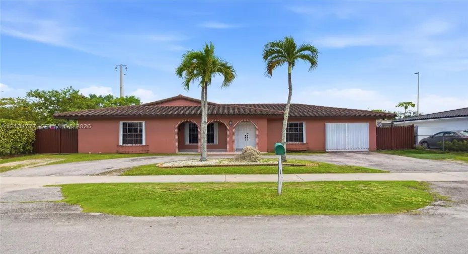 Mediterranean-style home featuring a terracotta tile roof, arched entryway, and dual palm trees