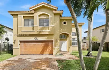 Two-story stucco exterior featuring a tiled roof, arched window detailing, a paved driveway, and a covered entryway